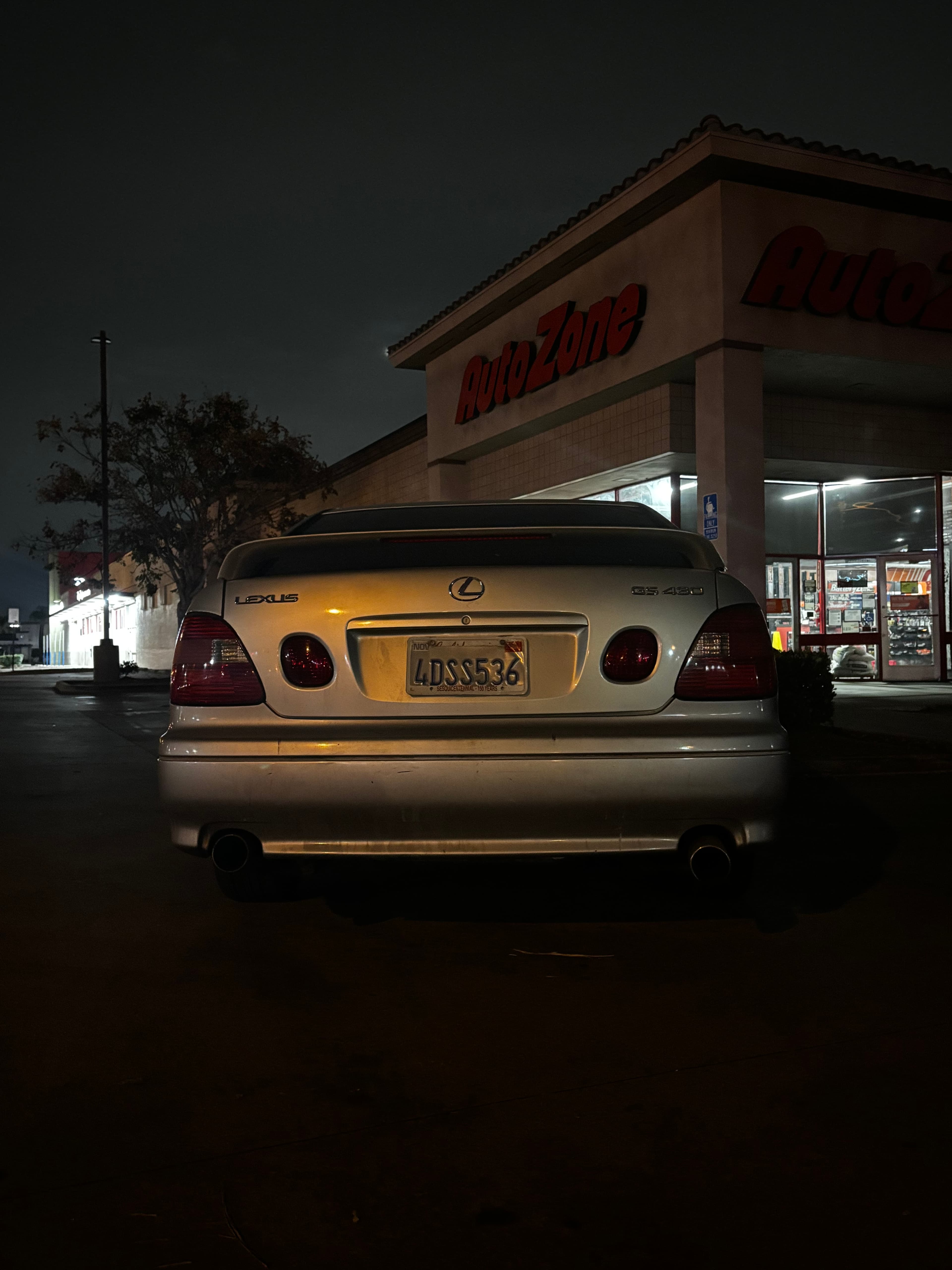 Rear view of a silver Lexus GS 430 parked outside an AutoZone store at night.