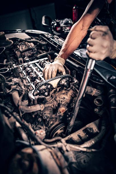 Mechanic's gloved hands using a long wrench to repair a complex, oily car engine.